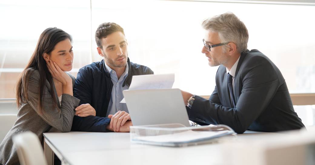 A couple study a document with a professional agent at a table with a laptop