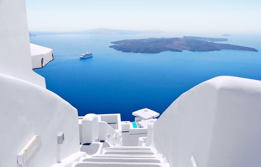 A sole motor yacht anchored in the bright blue waters off Mykonos viewed from a whitewashed hilltop villa