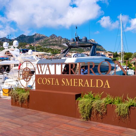 Sign reading Costa Smeralda with motor yacht charters berthed aft